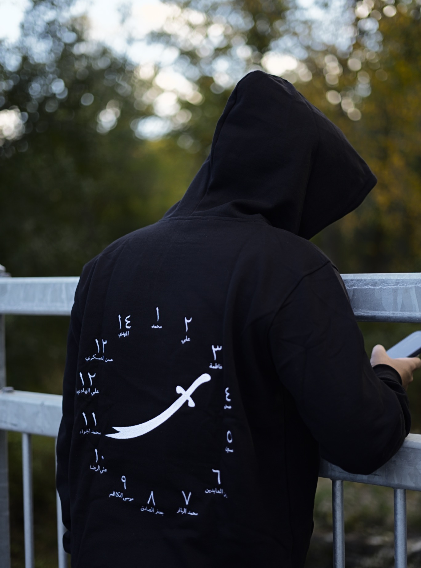 The 14 hoodie worn on a bridge, with white curved-sword and Arabic numeral artwork visible across the back