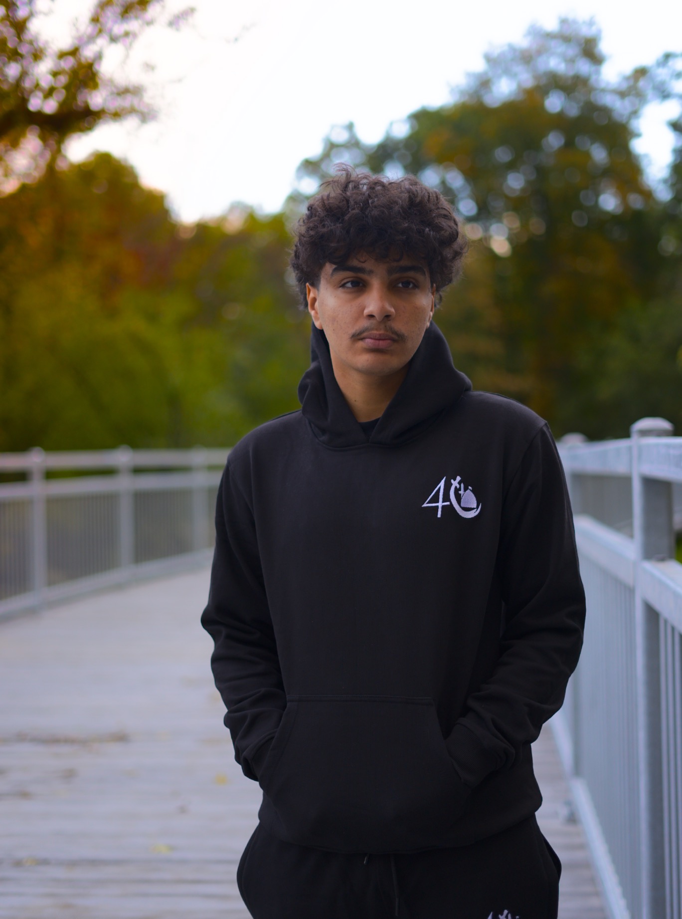 The 14 black hoodie worn facing forward on a bridge, showing the white chest emblem